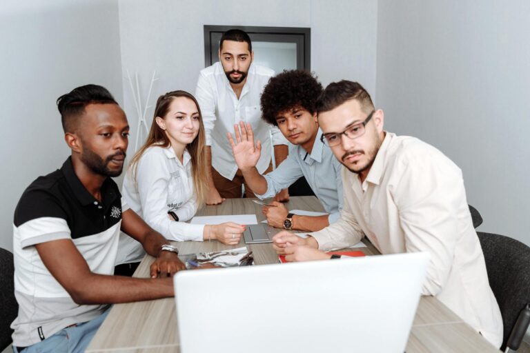Diverse team collaborating around a laptop in a modern office. Multi-ethnic group engaged in a team meeting.